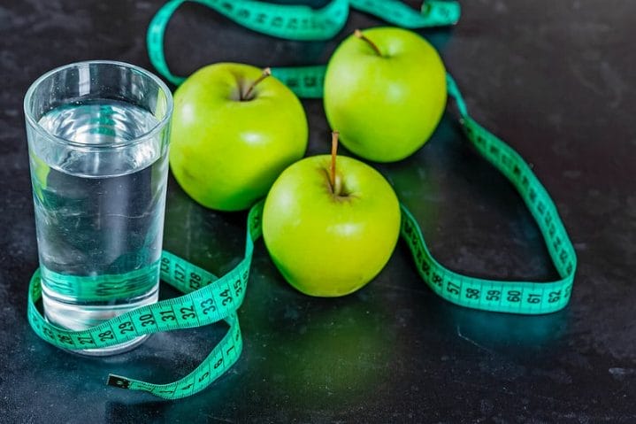 szklanka wody, zielone jabłka i centymetr krawiecki