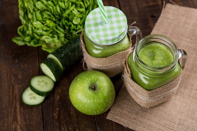 zielone smoothie w szklankach, obok zielone warzywa i owoce