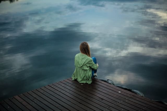 kobieta siedzi na skraju molo i patrzy w wodę