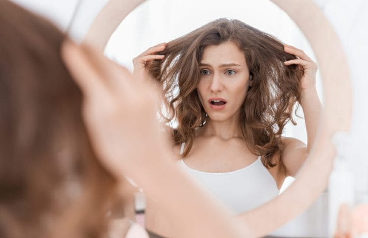 niezadowolona z wyglądu włosów kobieta patrzy w lustro 