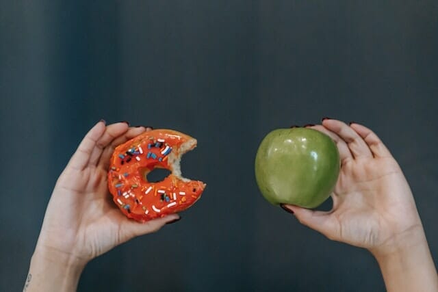 dwie dłonie, jedna trzyma jabłko, druga pączka